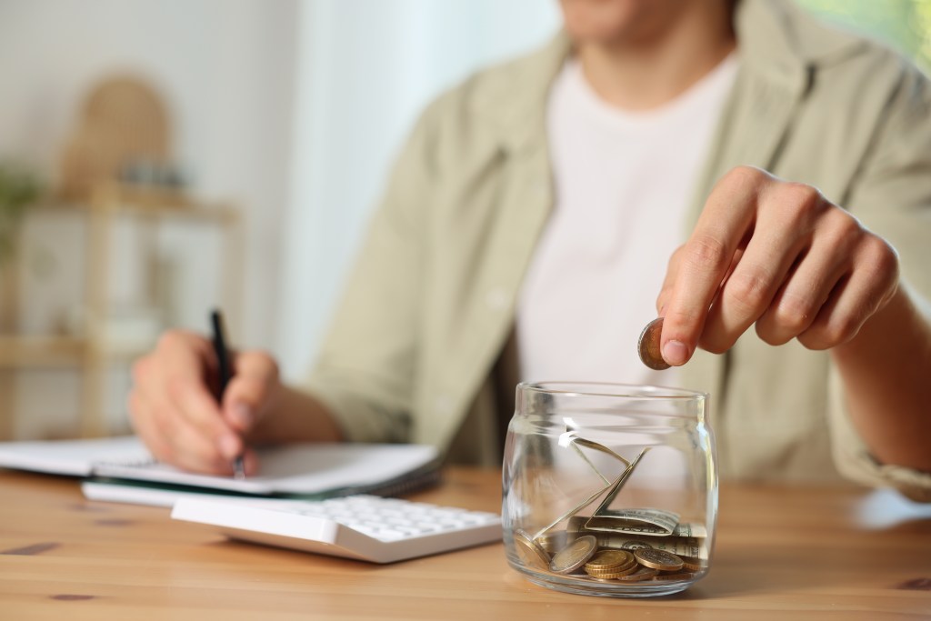 Person putting cash into emergency fund savings jar while reviewing budget and financial planning documents
