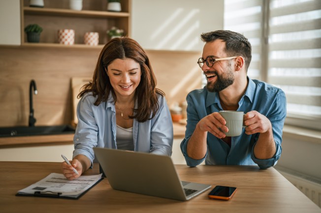 Parent and child planning a back-to-school budget at a kitchen table with a laptop and supplies.